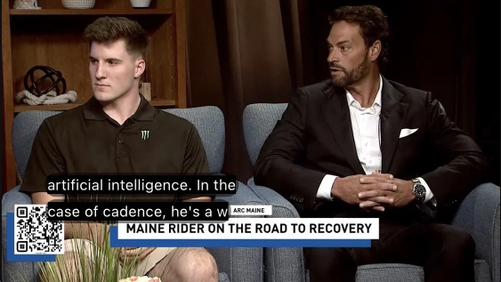 Two men seated on a talk show set with a lower third caption reading "Maine Rider on the Road to Recovery."