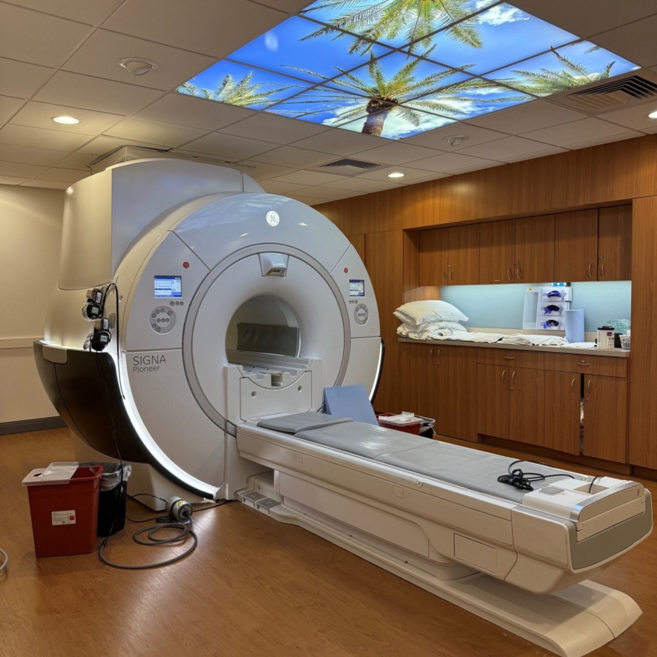 MRI machine in a medical facility with a decorative ceiling panel showing palm trees and a blue sky.