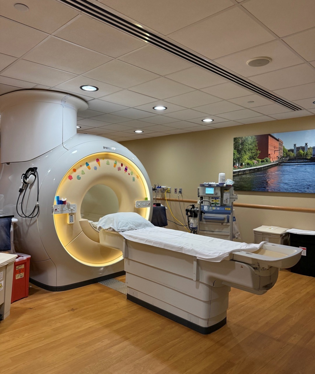 MRI machine in a hospital room with wooden flooring and medical equipment around.