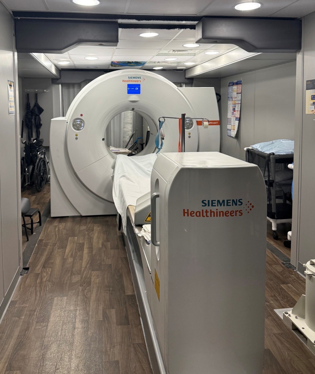 MRI machine in a medical facility scanning room with wooden flooring and equipment on the sides.