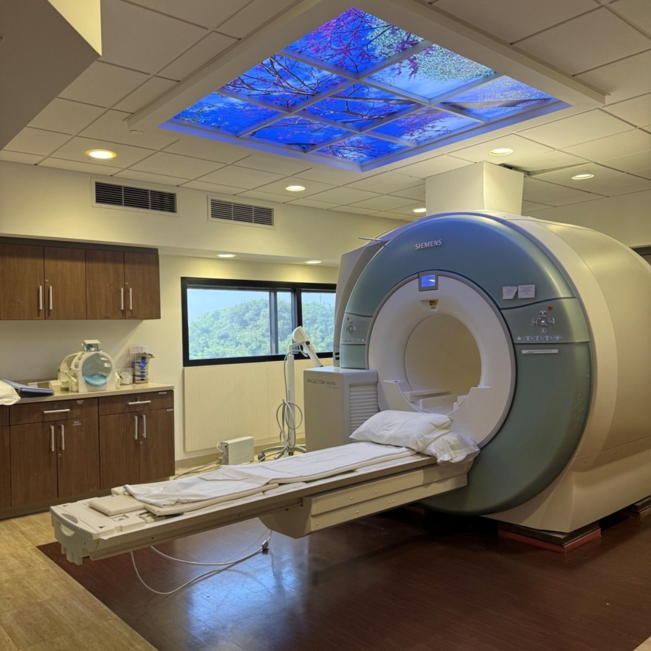 MRI machine in a modern, well-lit room with a nature-themed ceiling light panel.