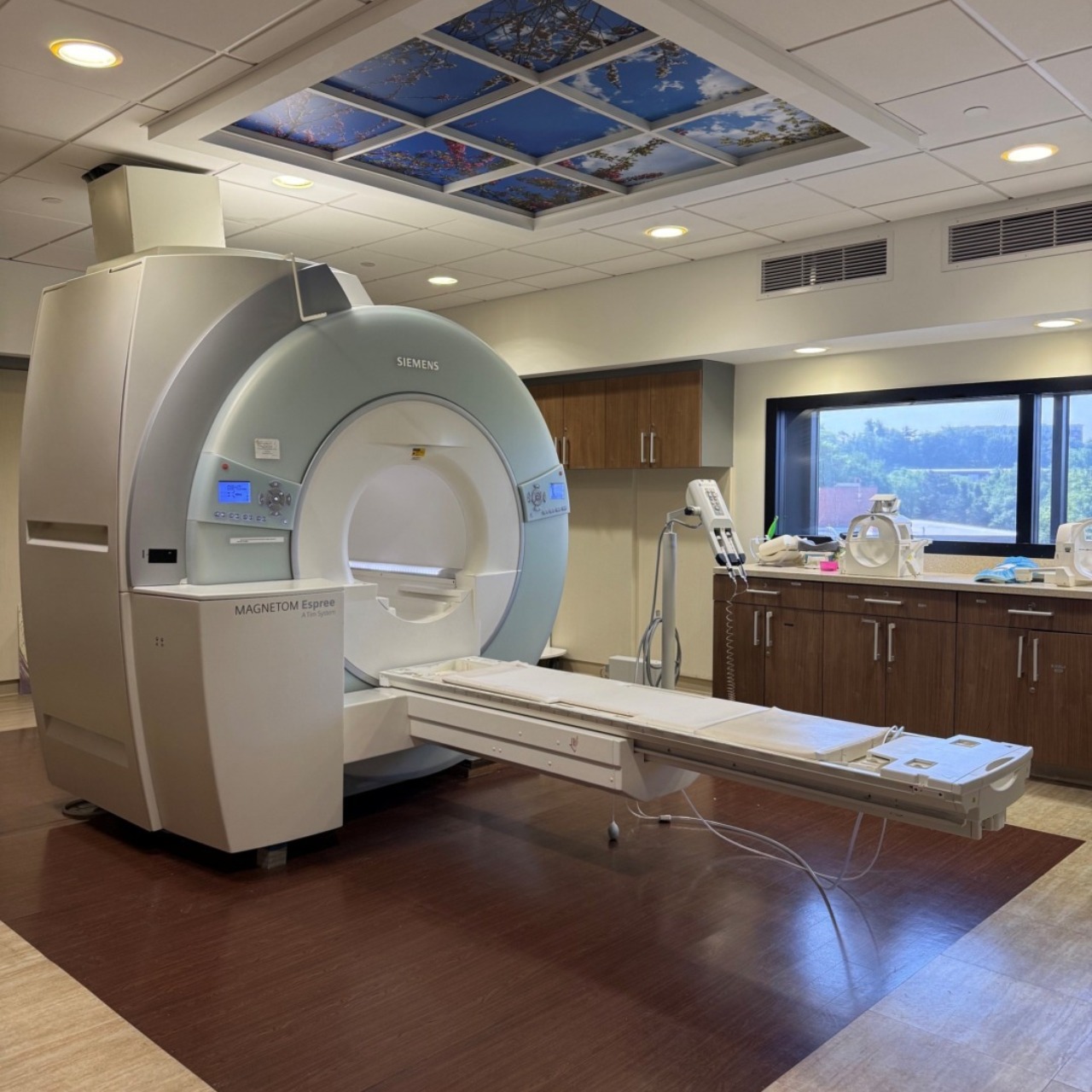 MRI machine in a hospital room with a scenic ceiling panel and window view.