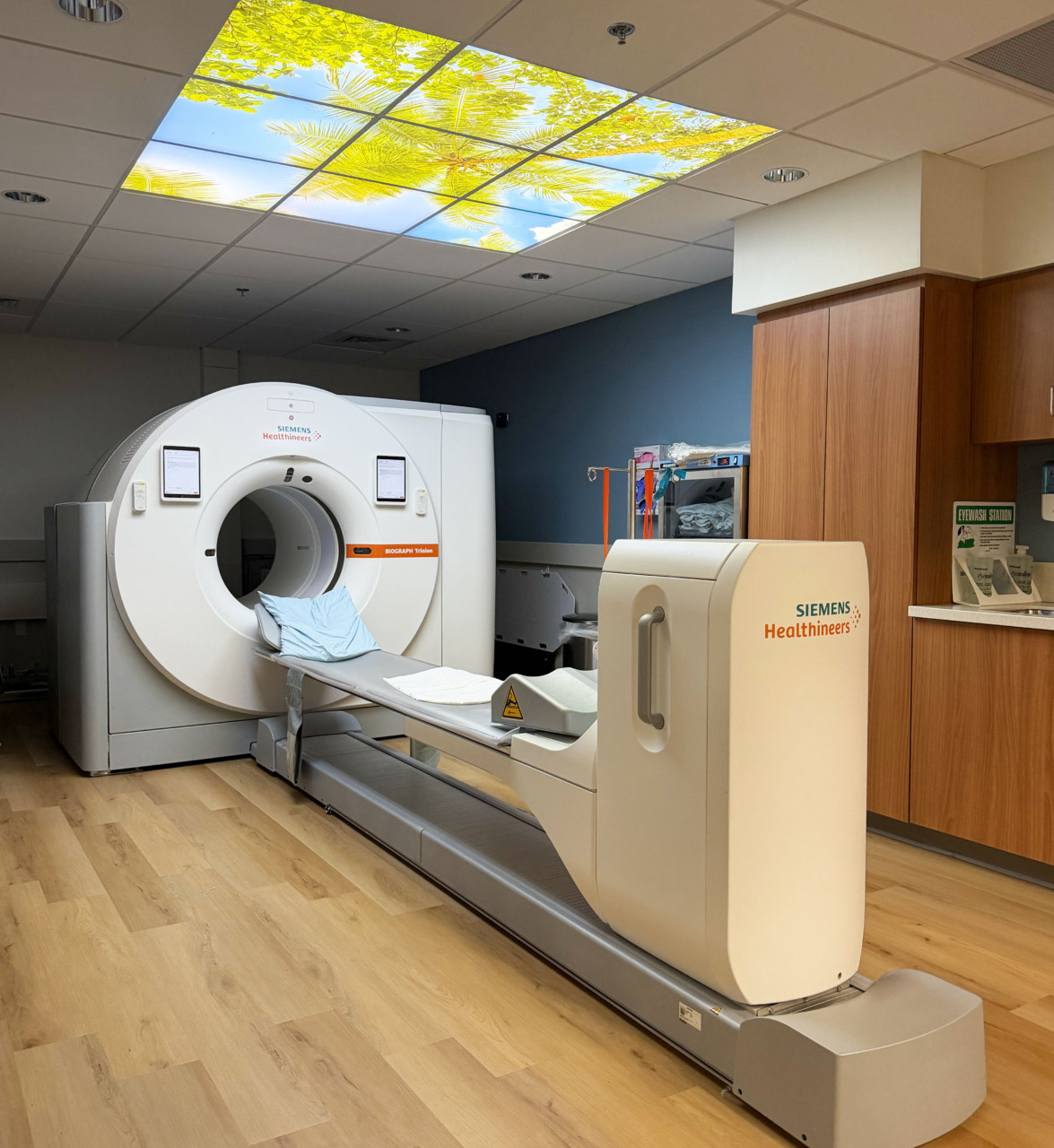PET/CT scanner in a suite with wood floor and ceiling art featuring sky and leaves for a calming atmosphere.
