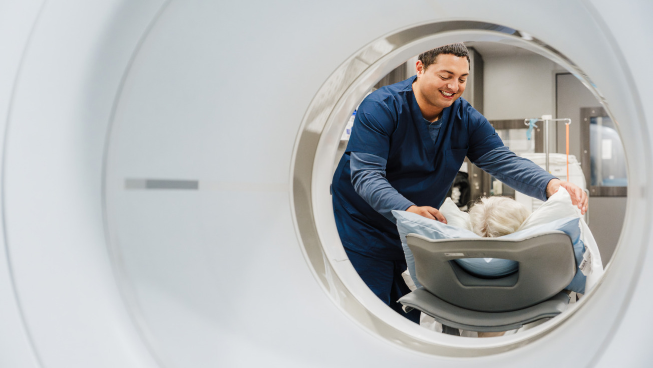 Radiologist assists elderly patient into MRI machine for a scan.