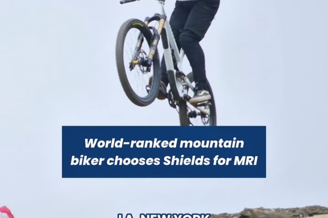 Mountain biker performing a jump off a rocky ledge with branded helmet and jersey, showcasing dynamic athletic skill.